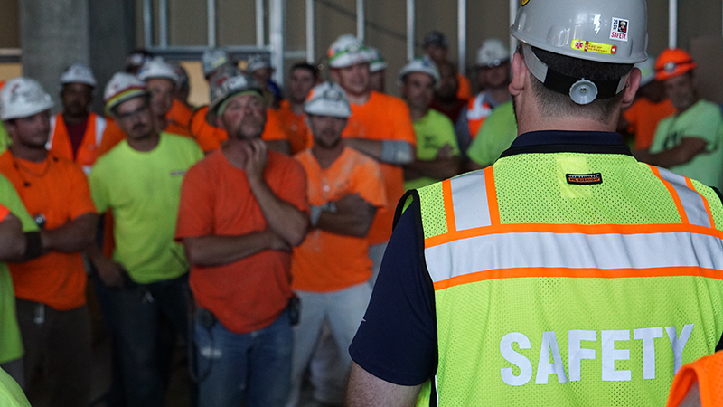 A group of construction workers listen as the safety lead conducts a meeting