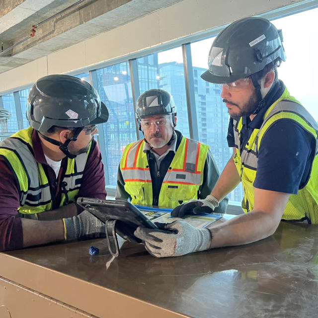 Three construction professionals discuss work plans on an iPad while leaning on a table